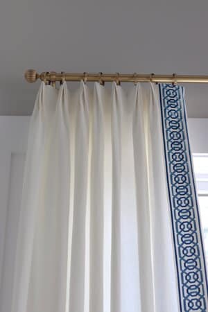 White curtains with blue trim on gold curtain rod.