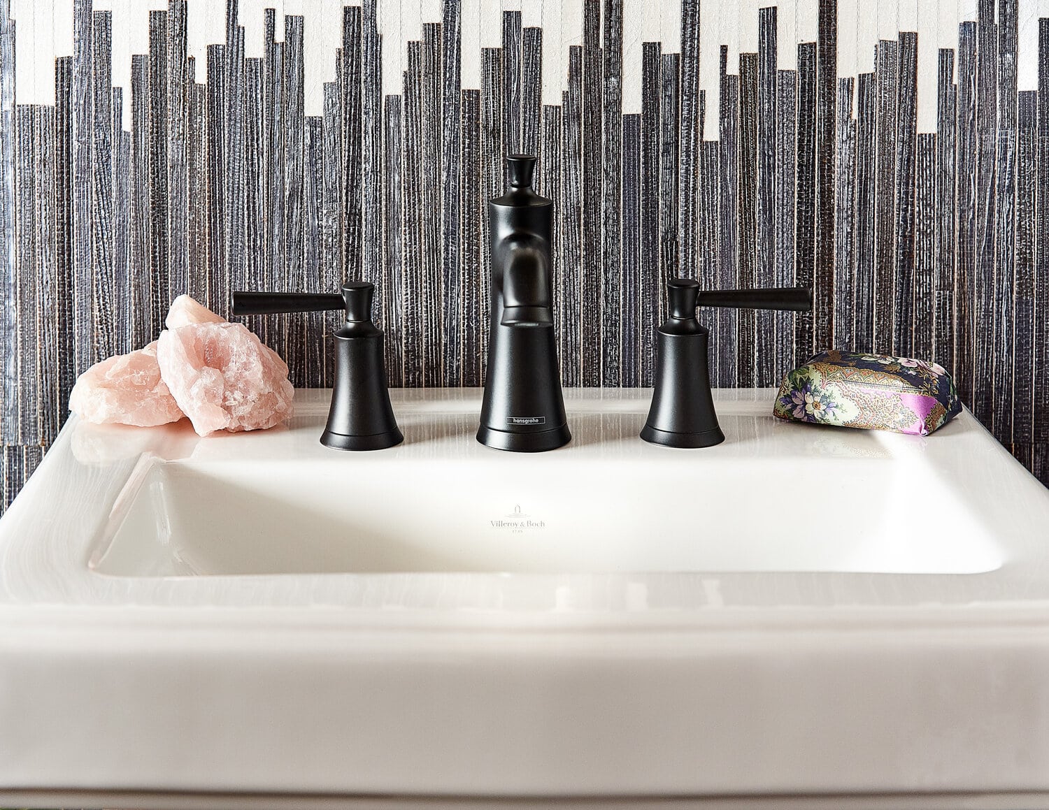 Modern bathroom sink with black fixtures and decorative tiles.