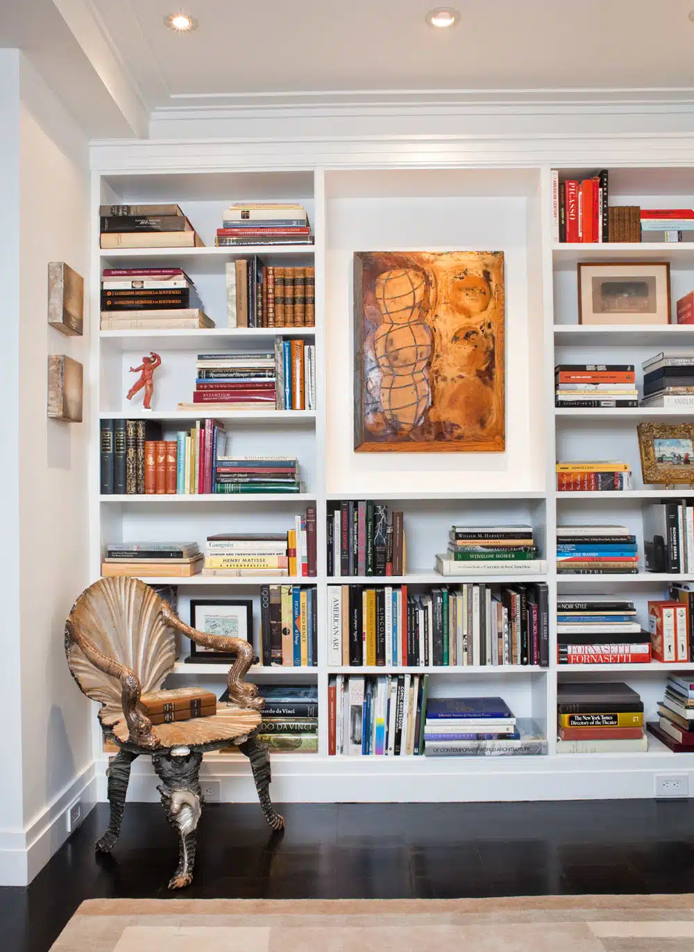 Elegant bookshelf with unique chair and artwork in home office.